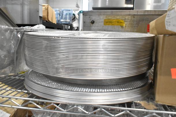 Brand new metal mesh pizza screens stacked on a shelf, part of a 42-item lot including metal bowl, stainless steel pans, and lids.