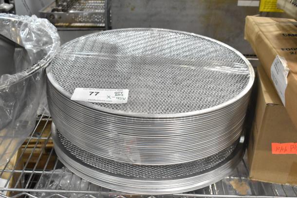 Brand new stack of metal mesh pizza screens with visible auction tag stating "77 QTY approx 42X PCIAuctions.com."