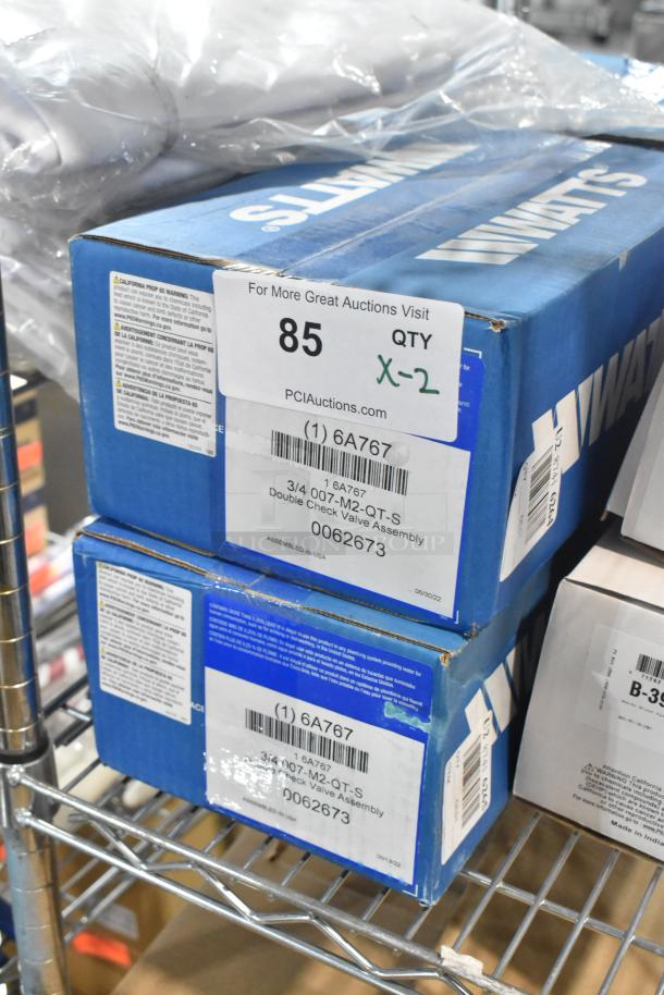 Two brand new Watts 007M2QTS-3/4 Double Check Valve Assemblies in original packaging, labeled with model and specifications.