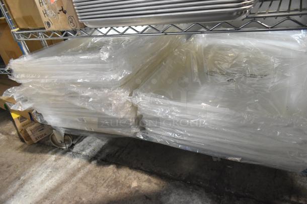 20 brand new Vollrath 9002CV full size NSF bun/sheet pan covers in plastic wrap, stacked on a metal rack.
