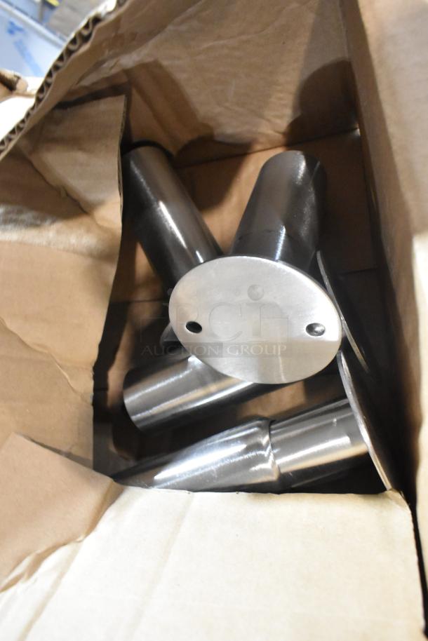 New metal legs in a cardboard box, showing a polished finish and drilled mounting holes. Four items included in bid.