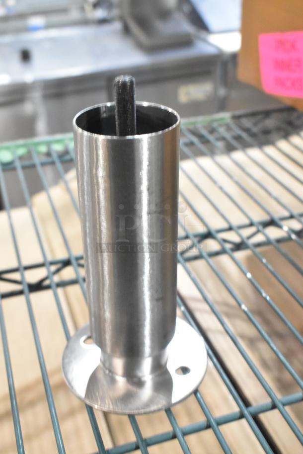 Metal leg on wire rack, brand new, cylindrical shape with flat base, drill holes for mounting, shiny finish.