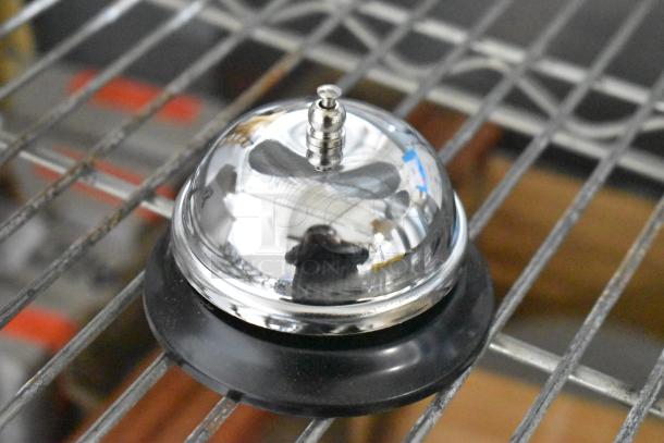 Brand new Tablecraft metal call bell on a shelf, shiny surface, black base. Part of a set of five, pristine condition.