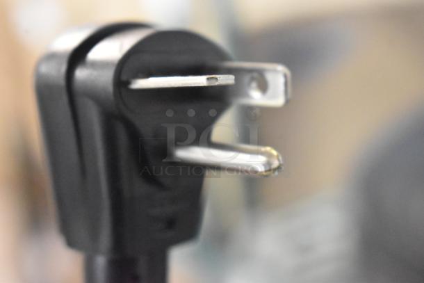 Close-up of a plug for the Amana RC17S2 commercial microwave oven, showing prongs and black casing, unused condition.