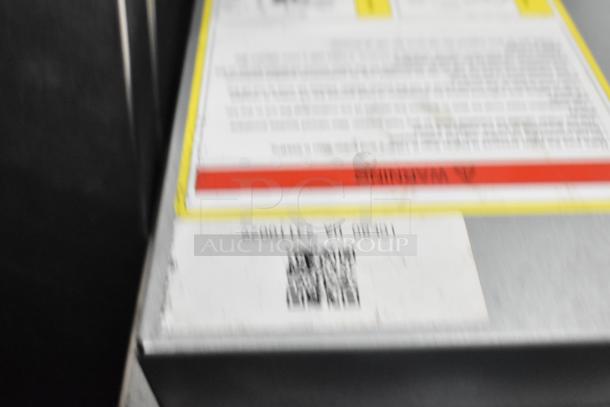 Blurry label on Coldline ICE80-HA ice machine displaying serial number and QR code. Stainless steel surface visible.