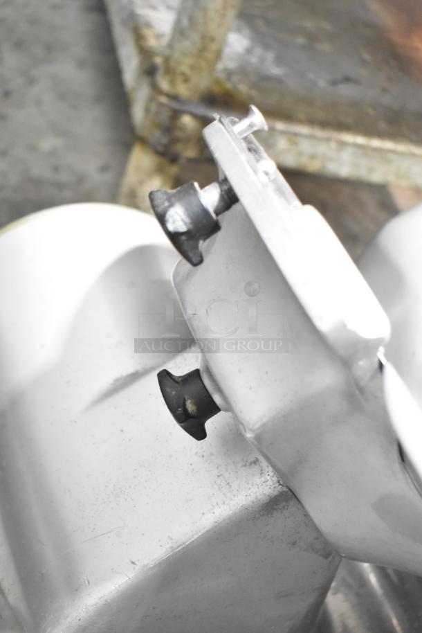 Metal commercial countertop meat slicer, 115 volts, 1 phase. Silver finish, visible screws, moderate wear, sturdy design.