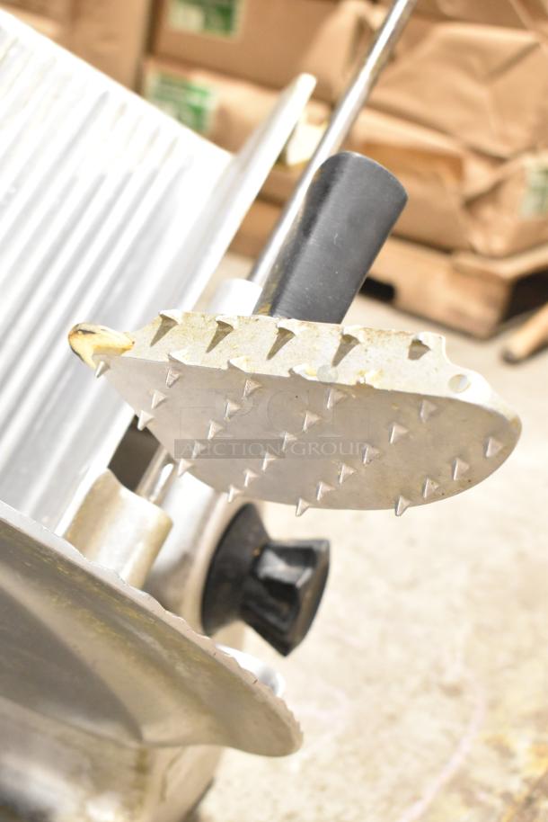 Metal commercial countertop meat slicer, 115 volts, 1 phase, features serrated blade and manual handle, moderate wear.