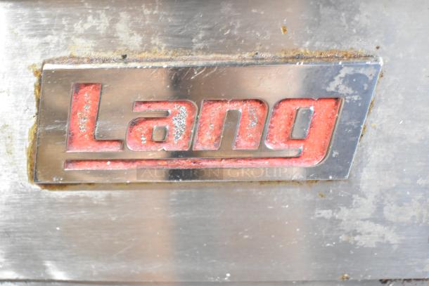 Lang stainless steel logo on commercial griddle, showing slight wear, indicating a durable, high-quality kitchen appliance.
