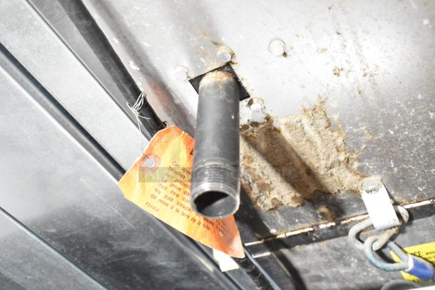 Close-up of the underside of Vulcan VC4GD-11D350K convection oven with attached inspection tag and visible pipe connection.