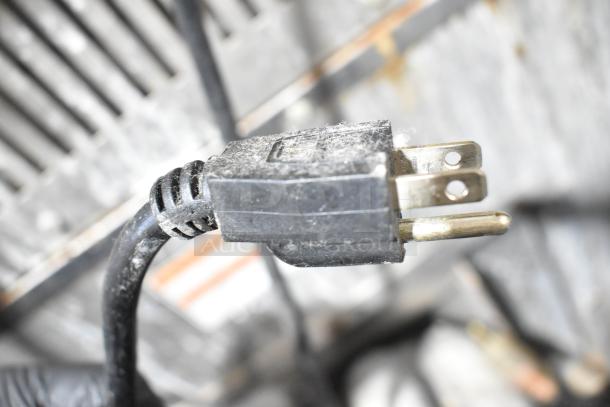 Black power plug with slight dust, attached to a cable, against a blurred industrial background.
