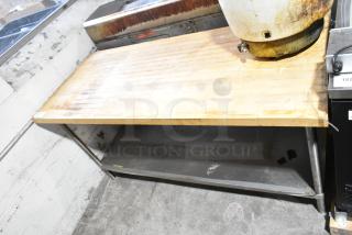 Wooden butcher block table with metal under shelf, showing wear. Ideal for kitchen prep. Marks suggest previous use.