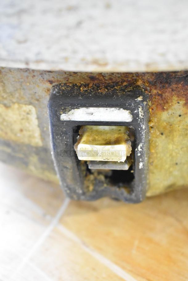 Close-up of a rusted metal countertop rice cooker switch. The cooker shows signs of heavy wear and corrosion.