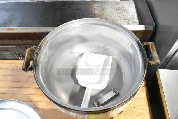 Metal countertop rice cooker with removable pot, showing signs of heavy use, includes a white serving scoop.