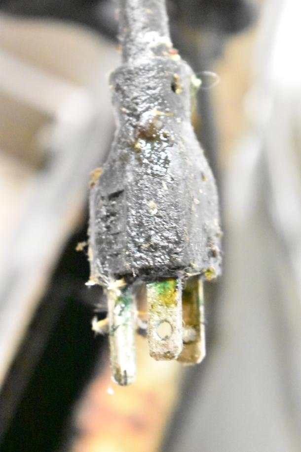 Close-up of a worn, greasy electrical plug with visible grime, likely belonging to a commercial appliance.