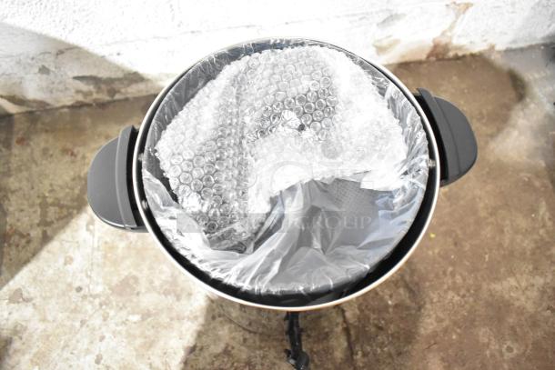 Stainless steel coffee urn with bubble wrap inside, new condition. Galaxy 100 Cup, 120V, 1,500W. Dual handles visible.