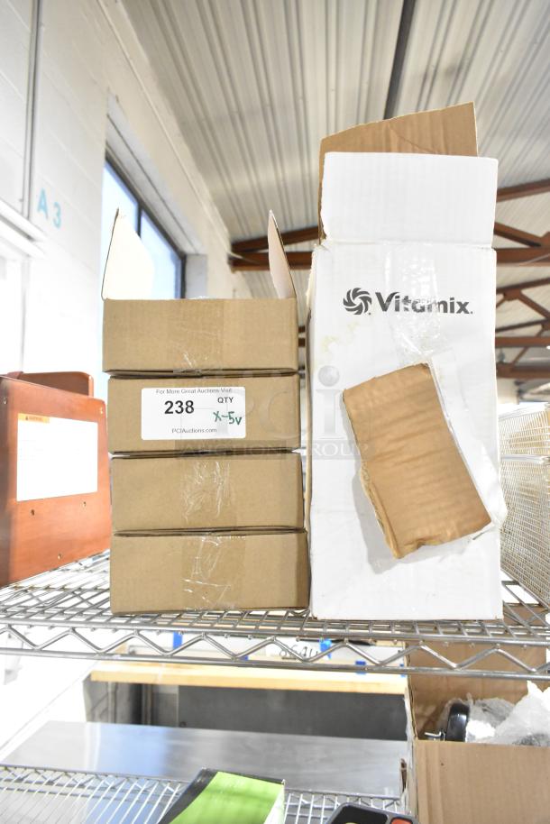 Five brand new boxes labeled "Vitamix" and others, with visible scratch and dent on packaging. Auction item with potential value.