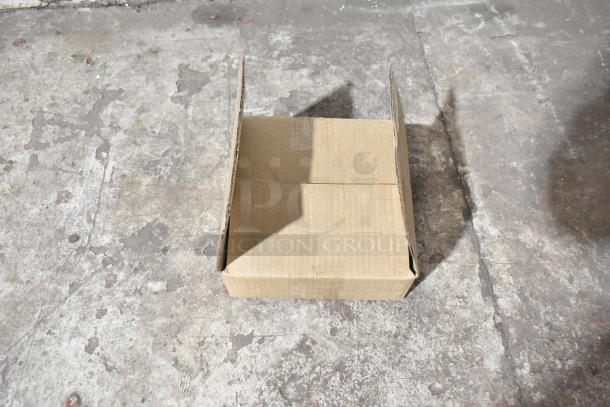 Empty cardboard box on concrete floor, possibly related to auction of 5 new scratch and dent items including VitaMix piece and plates.