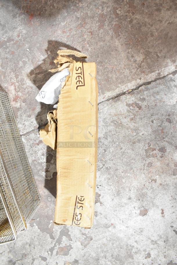 Cardboard box labeled "STEEL" with metal baskets, showing signs of wear, on concrete.