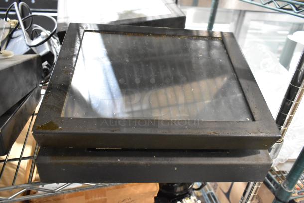 7 various POS monitors and receipt printers, used condition, stacked on metal shelving. Includes cords and accessories.