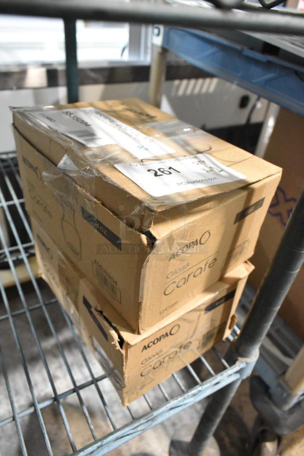 Two boxes of brand new, scratch and dent Acopa 4 oz. glass carafes on a metal shelf. Auction label reads "261".
