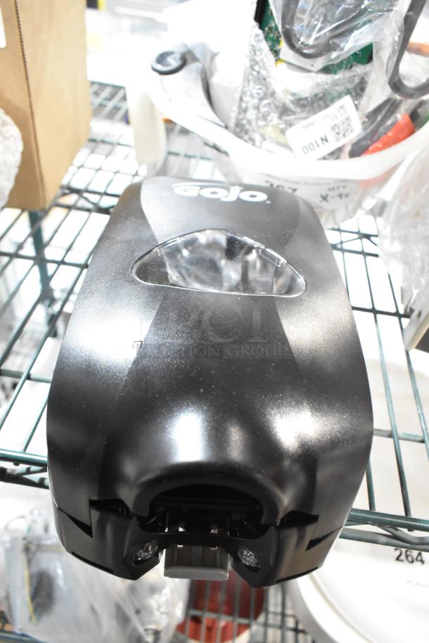 GOJO® TFX 1200 mL black touchless hand soap dispenser, model 2730-12, new, visible scratch, resting on metal shelf.