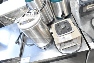 VitaMix VM0145 blender base with attached cables beside a 3-gallon stainless steel tank, in used condition. Auction label "276 X2".