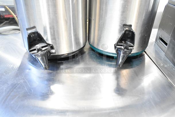 Two stainless steel beverage dispensers with black spouts, displayed on a reflective surface.