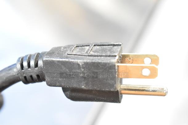 Close-up of a standard black electrical plug with two flat prongs and one round prong, for a 120-volt appliance.