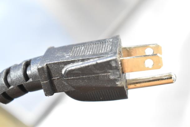 Close-up of a black power plug connected to the VitaMix VM0145 blender, showing two flat prongs and a round ground pin, designed for 120 volts, 1 phase.