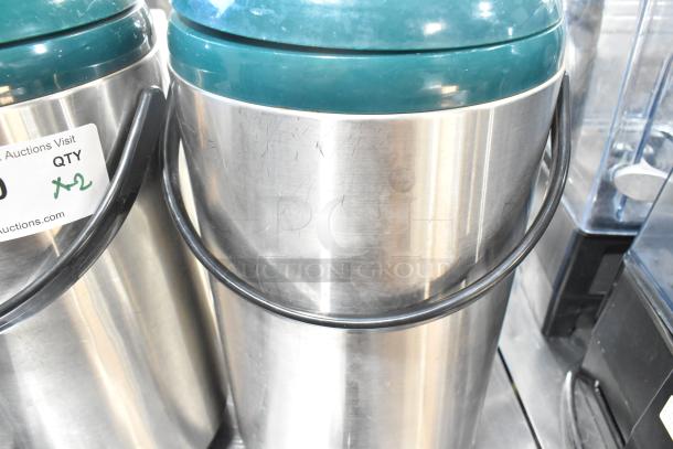 2 stainless steel beverage dispensers with green lids and handles, minor surface scratches, auction label indicating quantity of 2.