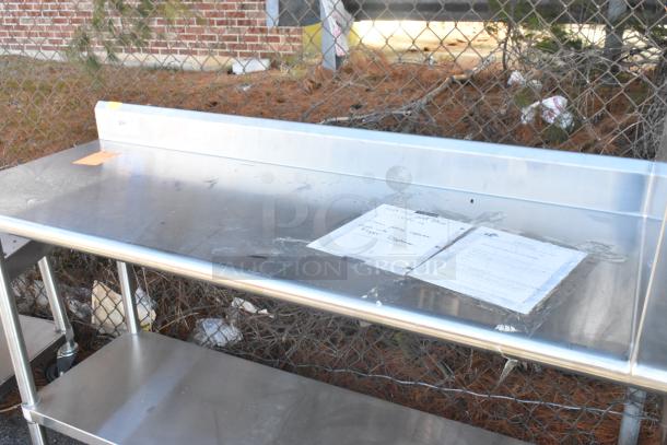 Stainless steel table with sink bay, backsplash, and under shelf. Includes documents taped to surface. Appears in good condition.