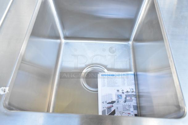 Stainless steel sink bay with visible under-shelf, clean surface, and document placed inside. Features a back splash.