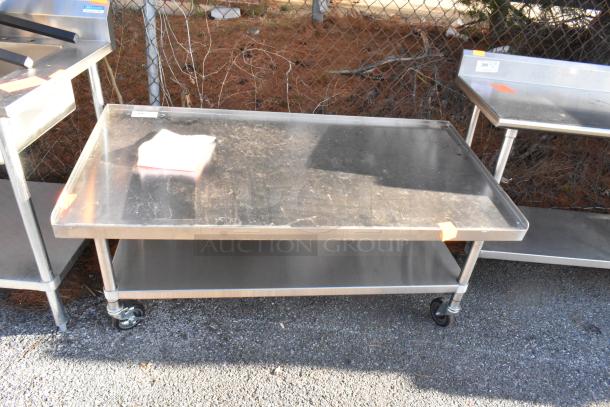 Stainless steel equipment stand with under shelf, commercial casters, showcasing slight wear, ideal for kitchen use.