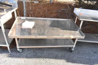 Stainless steel equipment stand with under shelf, commercial casters, showcasing slight wear, ideal for kitchen use.