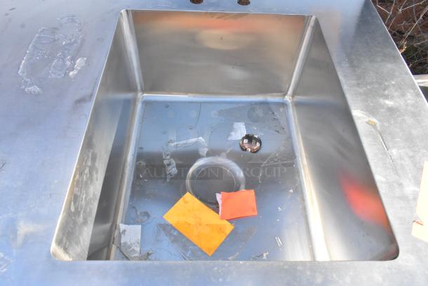 Stainless steel table with sink bay, backsplash, and under shelf. Used condition with visible wear and markings.