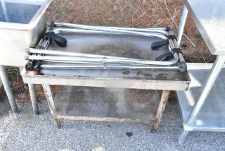 Metal table with under shelf, weathered condition, visible rust and discoloration, located outdoors with nearby metal items.