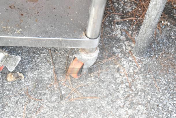 Stainless steel equipment stand with visible caster, slightly worn, used for supporting rice cookers; features under shelf.