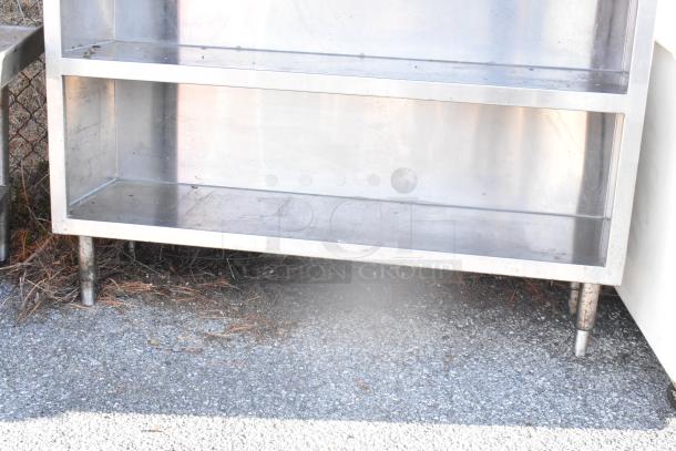 Stainless steel table with two under shelves, showing signs of wear. Ideal for storage and workspace efficiency.