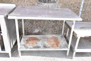 Stainless steel table with metal under shelf, visible rust and wear, equipped with a can opener mount, ideal for industrial use.