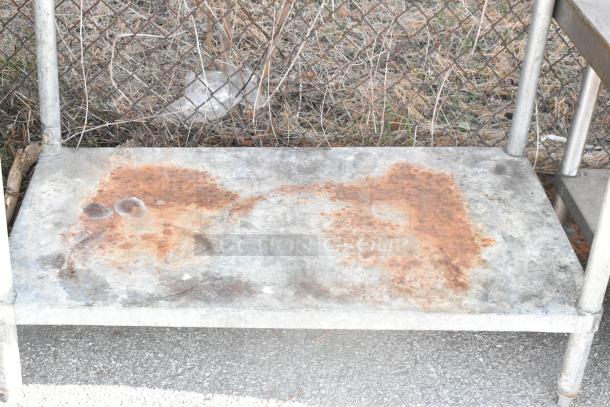 Stainless steel table with metal under shelf and can opener mount. Visible rust and wear. Mounted under shelf. Auction item.