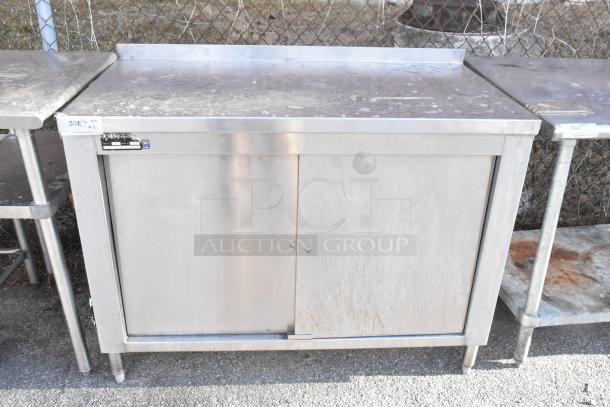 Stainless steel table with metal under shelves and sliding doors, some surface wear visible, industrial design.