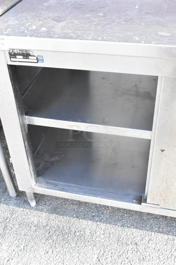 Stainless steel table with metal under shelves and doors, featuring visible wear. NSF certified label on top edge.