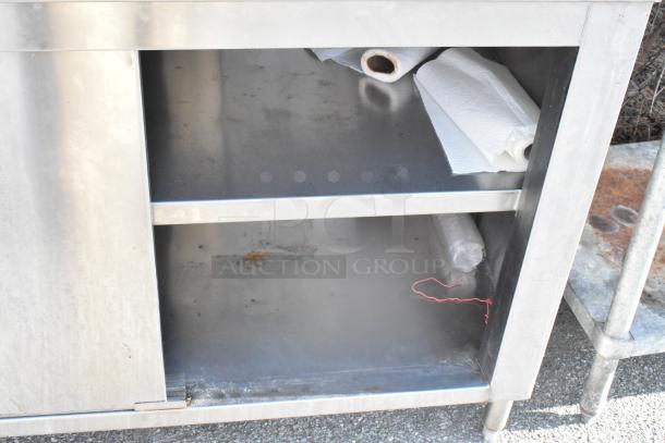 Stainless steel table with metal under shelves and sliding doors, moderate wear. Ideal for kitchen or industrial use.