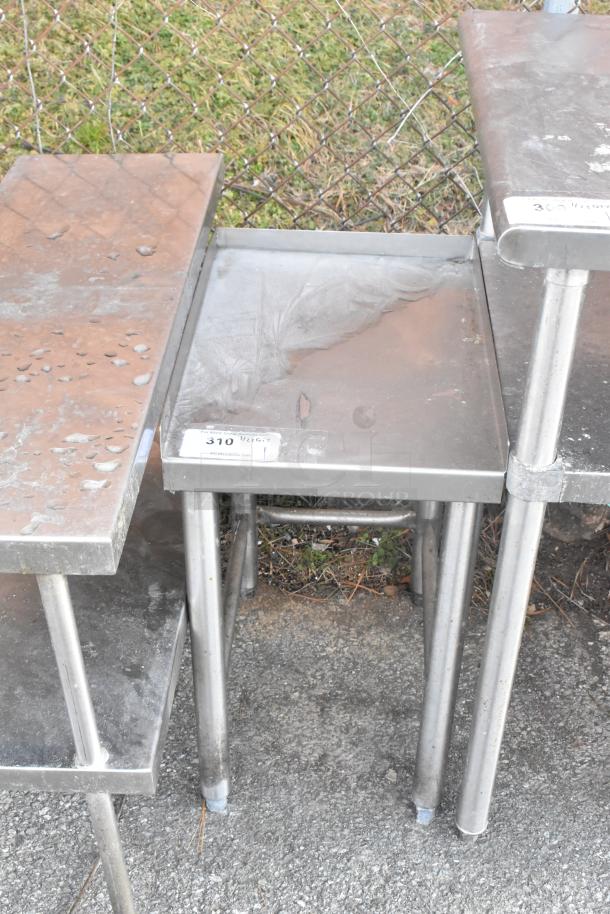 Stainless steel table showing signs of wear, marked "310 Peggy" with a label, sturdy metal legs.