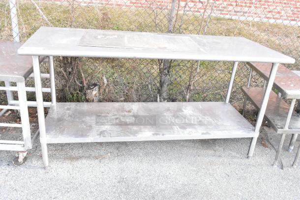 Stainless steel table with metal under shelf, outdoor setting. Used condition, visible surface marks. Perfect for commercial use.