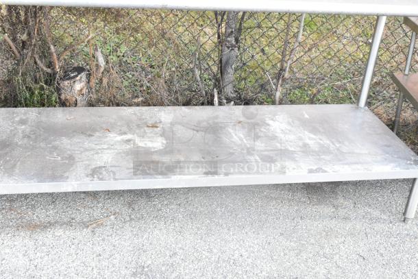 Stainless steel table with metal under shelf, weathered condition, suitable for kitchen or industrial use, outdoor setting.