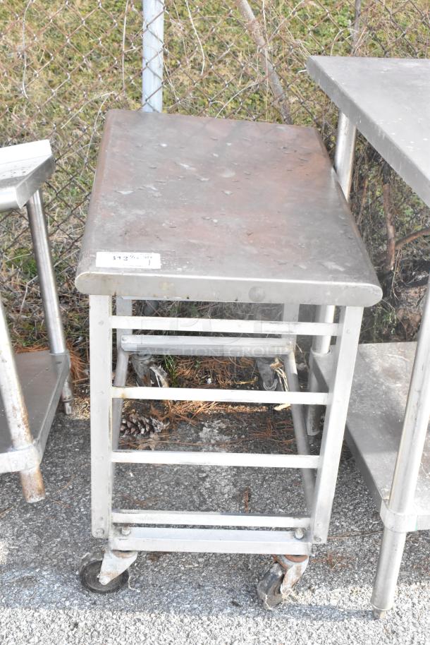 Metal pan rack on commercial casters, sturdy metal frame with multiple slots, some surface rust and wear visible. Tag reads "$13 8/26 312V".