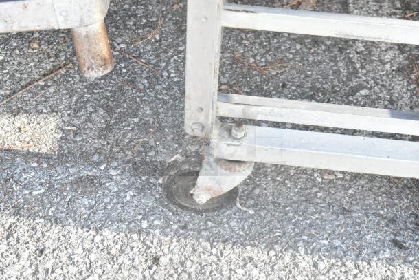 Metal pan rack with commercial casters, visible wear on wheels, suitable for kitchen use and easy mobility on uneven surfaces.
