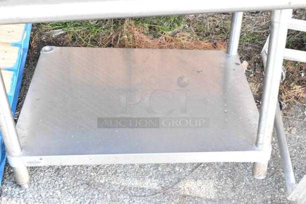 Stainless steel table with metal under shelf, sturdy construction, visible wear, suitable for industrial or kitchen use.