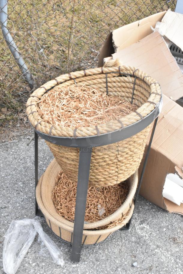 Metal stand with two rope-woven baskets, filled with shredded paper. Baskets are stacked; stand is black metal. Slight wear visible.